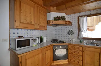 a kitchen with wooden cabinets and a stove and a microwave at Holidays on Dolomites in Villanova