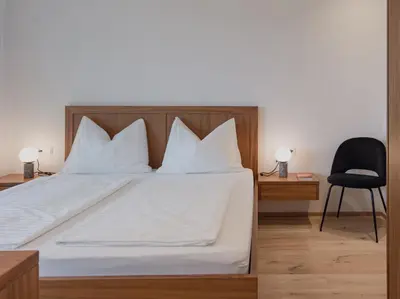 a bedroom with a bed with white sheets and a black chair at The Hills Merano in Merano