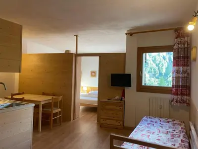 a bedroom with wooden walls and a kitchen in the background at Casa Pisolo - presso Sussy Residence in Falcade