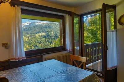a room with a table and two large windows at Appartamento Pepe by Sunhome Fiemme in Castello di Fiemme