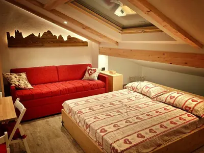 a bedroom with a bed and a red couch at Ad Alba di Canazei una finestra sulla Marmolada in Alba di Canazei