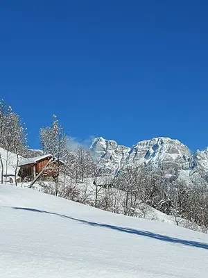 a snow covered slope with a house and mountains in the background at LA POESIA DOLOMITI APARTMENTS in Rivamonte
