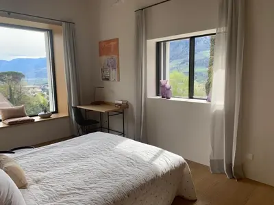 a bedroom with a bed and a desk and two windows at Villa Tschaupp in Tirolo