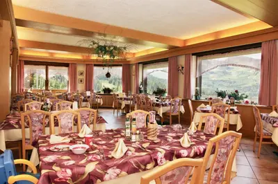 a dining room with tables and chairs and windows at Albergo Venezia in Passo Rolle