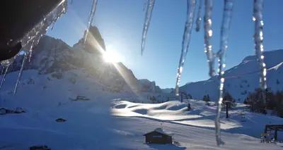 a ski lift with the sun shining on a snow covered mountain at Albergo Venezia in Passo Rolle