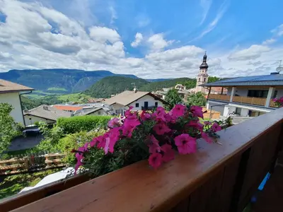 a balcony with pink flowers on a wooden railing at B&B Garni Lantschner in Kastelruth