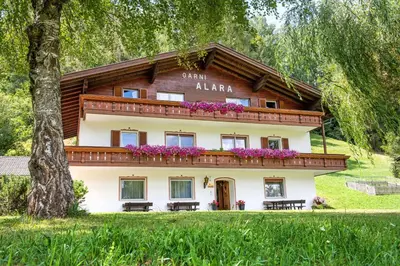 a house in the woods with purple flowers at Alara Rooms in Ortisei