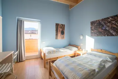 two beds in a blue room with a window at Hostel L'Ost - Ostello di Grumes in Grumes