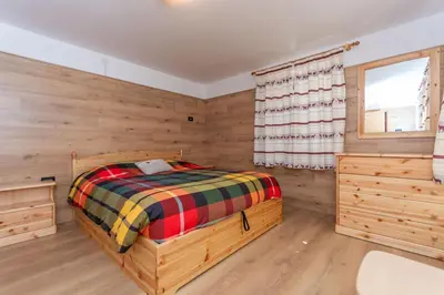 a bedroom with a bed and a window and wooden walls at Casa Caviola Centro in Falcade