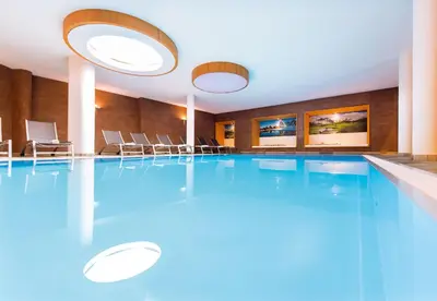 a swimming pool in a hotel room with blue water at Hotel DAS ROYAL in Obereggen in Obereggen