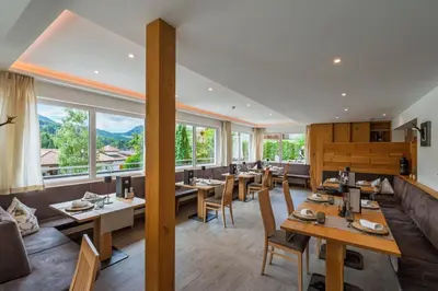 a restaurant with wooden tables and chairs and large windows at Hotel DAS ROYAL in Obereggen in Obereggen
