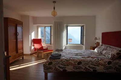 a bedroom with a bed and a chair and windows at Civetta panoramic mountain home in Alleghe