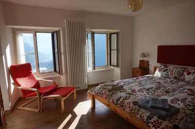 a bedroom with a bed and a chair and windows at Civetta panoramic mountain home in Alleghe