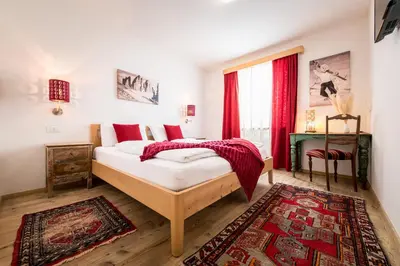a bedroom with a bed with red curtains and a rug at Am Schloss Guest House in Brunico