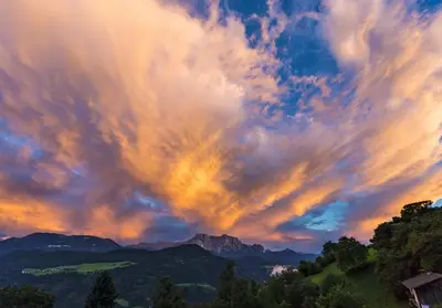 a cloudy sky at sunset with mountains and trees at Fössing Hof.Apartment in Barbiano