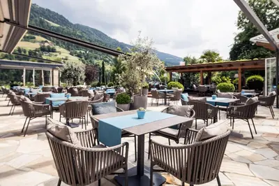 a restaurant with tables and chairs with mountains in the background at Hotel Chalet Das Alpenschlössel in Saltusio