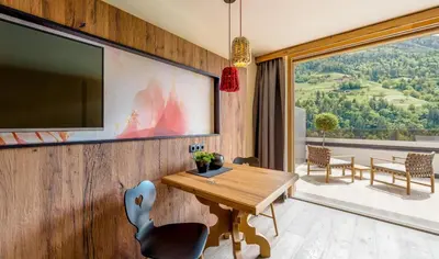 a dining room with a wooden table and a large window at Hotel Chalet Das Alpenschlössel in Saltusio