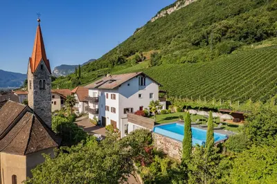 an estate in a vineyard with a swimming pool and a church at Runggnerhof in Termeno