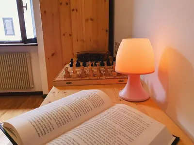 a lamp and an open book on a table next to a chessboard at Oasi Verde - Alpine Stay Apartments in Carano