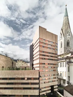 a tall building next to a church with a steeple at Boutique Hotel Badhaus in Bressanone