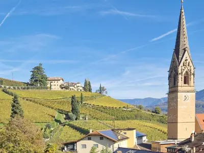 a church with a steeple on a hill with vineyards at Langenmantel Historic Suites in Termeno