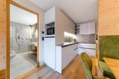 a kitchen with white cabinets and a sink and a shower at Rienz Alpine City Suites in Brunico