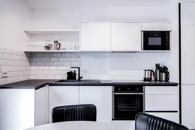 a white kitchen with white cabinets and black appliances at Apartmenthouse STERN in Vipiteno