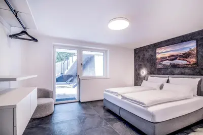 a white bedroom with a bed and a kitchen at Apartmenthouse STERN in Vipiteno