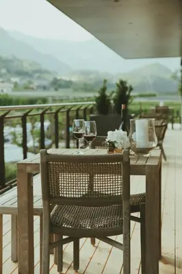 a wooden table with chairs and wine glasses on a balcony at Solterra Poolhouse 2 in Tisens