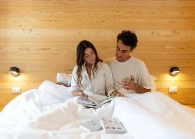 a man and woman sitting in bed reading a book at Chalet Le Grazie in Le Grazie