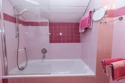 a bathroom with a tub and a shower with pink tiles at Apartment Obkircher in Nova Levante