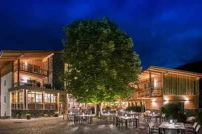 a building with tables and chairs in front of a tree at Hotel Gasthof Höllriegl in Sarntal