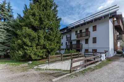 a white building with a wooden fence and trees at Casa Baranci in Pozza di Fassa