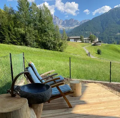 a chair on a wooden deck with a grill and mountains at Farmhouse with a stunning view over the dolomites in Villnoss