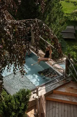 a woman sitting on a bench in a swimming pool at Lusina Apartments in Luson