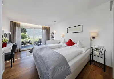 a white bedroom with a bed and a desk and a window at Pension Riedingerhof in Merano