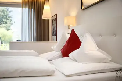 two white beds with red pillows in a hotel room at Pension Riedingerhof in Merano