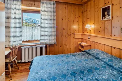 a bedroom with a bed and a desk and a window at Appartamenti Pagan in San Vito di Cadore