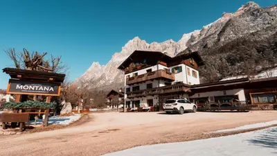 a building in the mountains with a car parked in front at Appartamenti Pagan in San Vito di Cadore