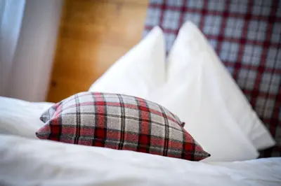 a plaid pillow on a bed with white pillows at Appartements Kirchtalhof in Lana