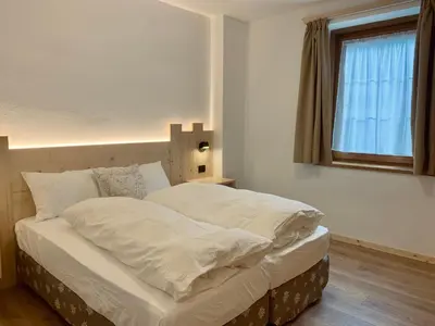 a bedroom with a bed with white sheets and a window at Cesa Do Ruf eurochalet in Campitello di Fassa