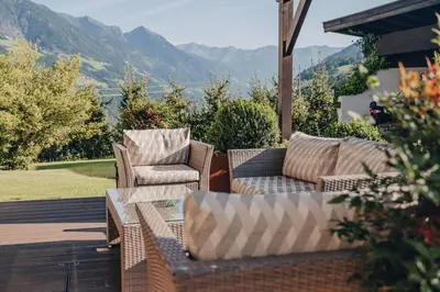 two chairs and a table on a patio with mountains at Hotel Schönbrunn in Schenna
