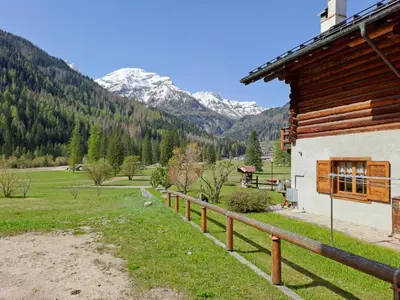 a building with a fence next to a field and mountains at Tabia Maredane in Falcade