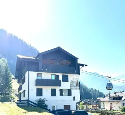 a white building with a black roof and a ski lift at Cesa Balzan in Canazei