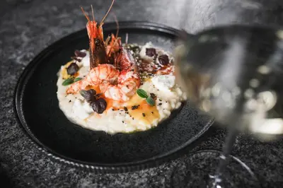 a plate of food with shrimp and a glass of wine at SomVita Suites in Tirolo