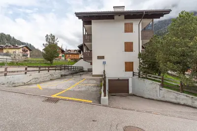 a white building with a garage in a parking lot at Casa Ciadenac in Soraga