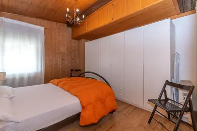 a bedroom with a bed with an orange blanket and a chair at Casa Bristol in Pozza di Fassa