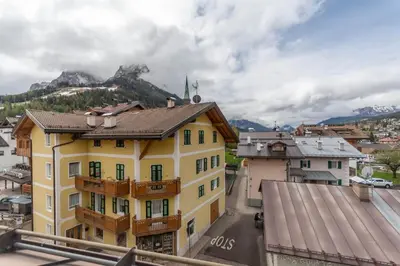 a yellow building with a balcony and mountains in the background at Casa Bristol in Pozza di Fassa