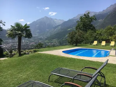 a pool with chairs and a palm tree and mountains at Garden Apartment Villa Corazza in Tirolo