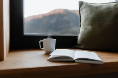a book and a coffee cup on a table with a window at Stricker Aparthotel in Tirolo